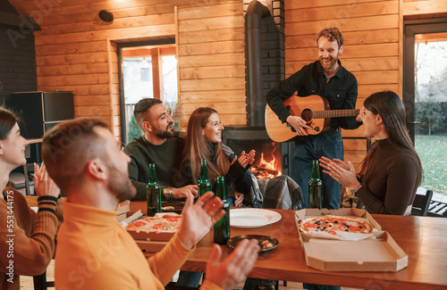 Green bottles with beer and pizza. Group of friends is having good weekend indoors in the wooden building together