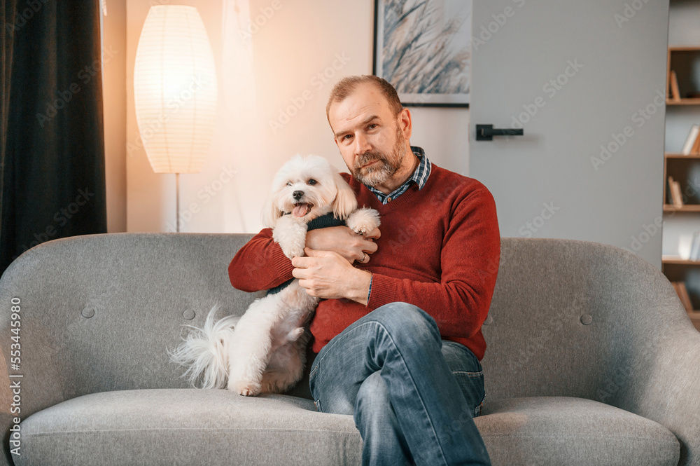 Man is sitting with his maltese dog on the sofa indoors Man is sitting with his maltese dog on the sofa indoors