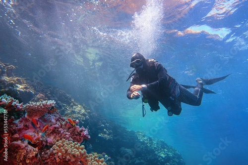 Fényképezés Man scuba diver descending from the sea surface to the colorful tropical coral reef