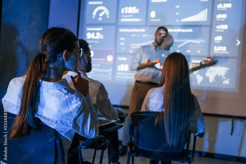 Master class. Male leader talking to employees, showing the plan on the projector in office of stock exchange company Master class. Male leader talking to employees, showing the plan on the projector in office of stock exchange company