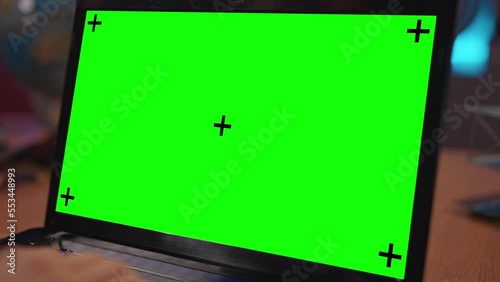 Old fashioned laptop with green screen standing on a desk in an office. Hands typing on computer with tracking points. Dark office. Creative people can put their own picture or video.
