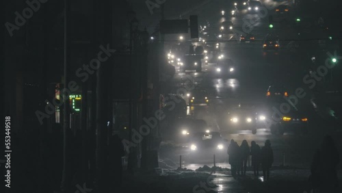 City traffic in the evening. Night city street with pedestrians and cars passing. Traffic in the night city with car lights and pedestrians passing by