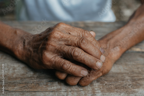 Close-up of old man's hands resting on wood. © NINENII