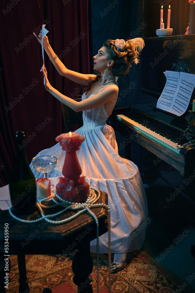 Obraz premium Portrait of young girl in image of medieval princess in white dress emotionally looking at music notes. Affectionate melody. Comparison of eras, beauty, history, art