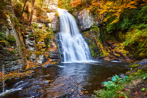 Fall foliage surrounds cliffs and huge waterfall over cliffs in peak fall