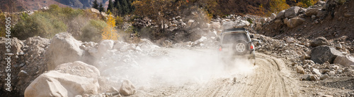 White SUV car climbs a dusty road in the mountains, banner ratio.