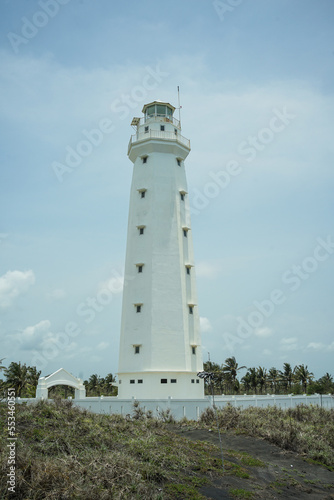 A lighthouse on the beach painted white against a blue sky background