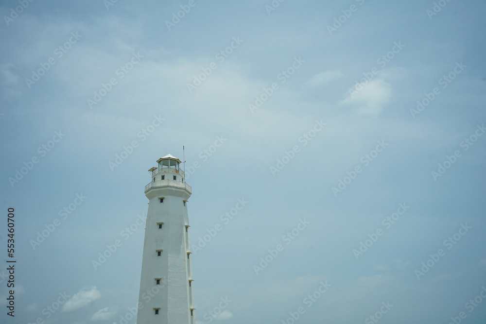 A lighthouse on the beach painted white against a blue sky background A lighthouse on the beach painted white against a blue sky background