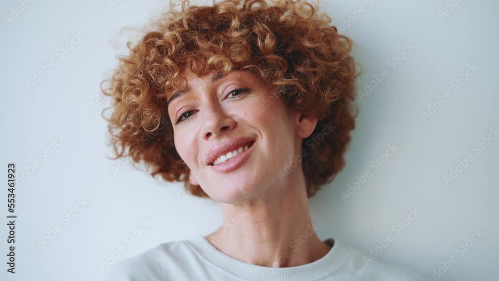 Focused adult curly haired woman looking at the camera in the grey studio Focused adult curly haired woman looking at the camera in the grey studio