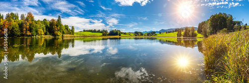 panoramic view to lake with symmetric reflection of sun on sky photo