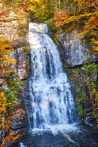 Straight on huge waterfall over cliffs with harsh light and fall foliage around