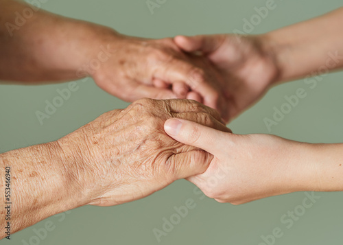 Elderly wrinkled and young hands hold together isolated on light green background