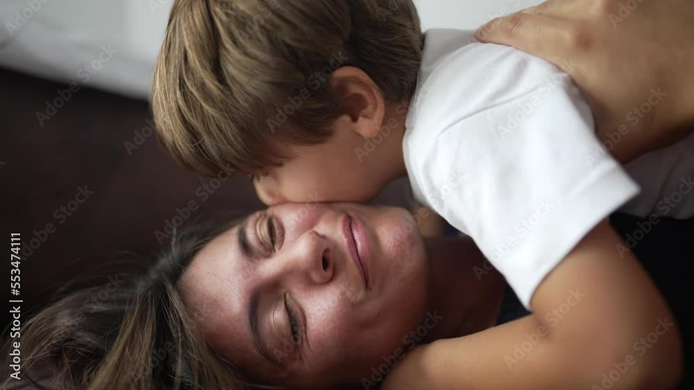 Child embracing mother lying on sofa indoors. Small boy laid on top of mom hugging. Parent and kid care affection concept Child embracing mother lying on sofa indoors. Small boy laid on top of mom hugging. Parent and kid care affection concept