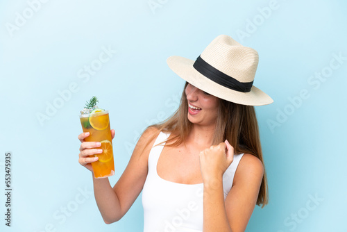 Young beautiful woman holding a cocktail isolated on blue background celebrating a victory