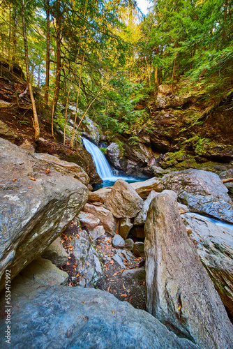 Large boulders near stunning waterfall with blue waters and cliffs covered in fall trees