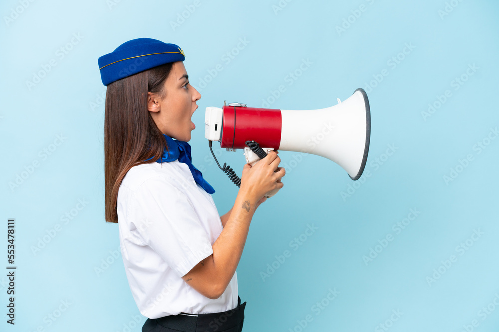 Airplane stewardess caucasian woman isolated on blue background shouting through a megaphone Airplane stewardess caucasian woman isolated on blue background shouting through a megaphone