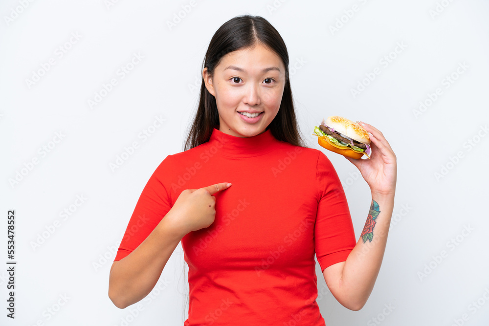 Young Asian woman holding a burger isolated on white background with surprise facial expression Young Asian woman holding a burger isolated on white background with surprise facial expression