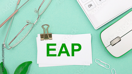 On a light green background there is a white calculator, a computer mouse, green leaves of a plant, gold-rimmed glasses and a white card with text EAP Employee Assistance Program. Business concept photo