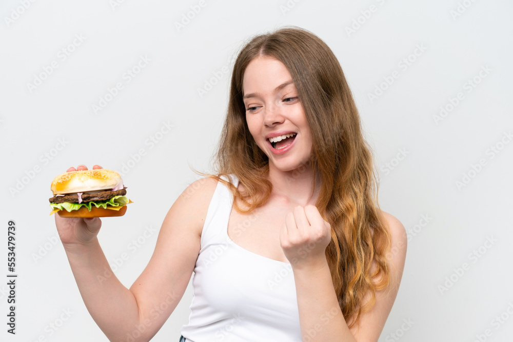 Young pretty woman holding a burger isolated on white background celebrating a victory Young pretty woman holding a burger isolated on white background celebrating a victory