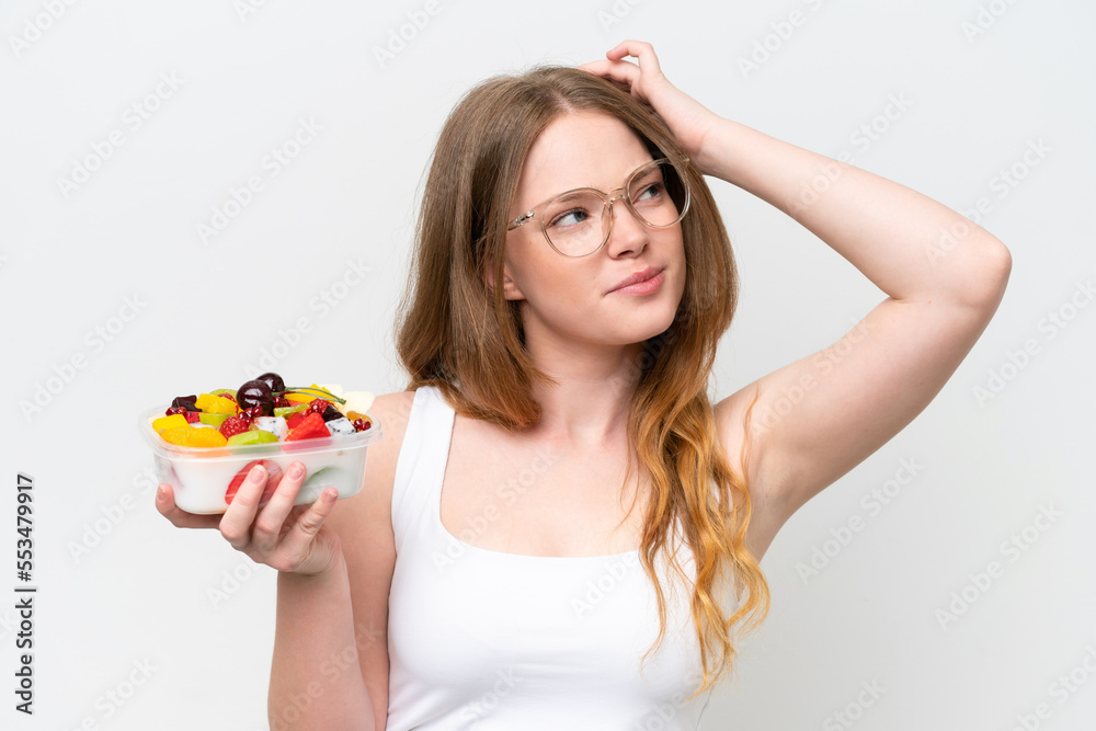 Young pretty woman holding a bowl of fruit isolated on white background having doubts and with confuse face expression Young pretty woman holding a bowl of fruit isolated on white background having doubts and with confuse face expression