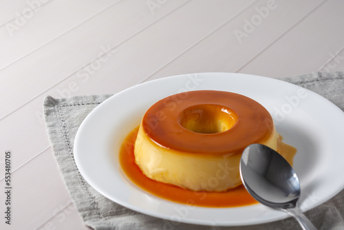 pudim de leite, also known as flan or milk pudding, isolated on white table with grey cloth. bitten slice with a metallic spoon concept of traditional brazilian dessert