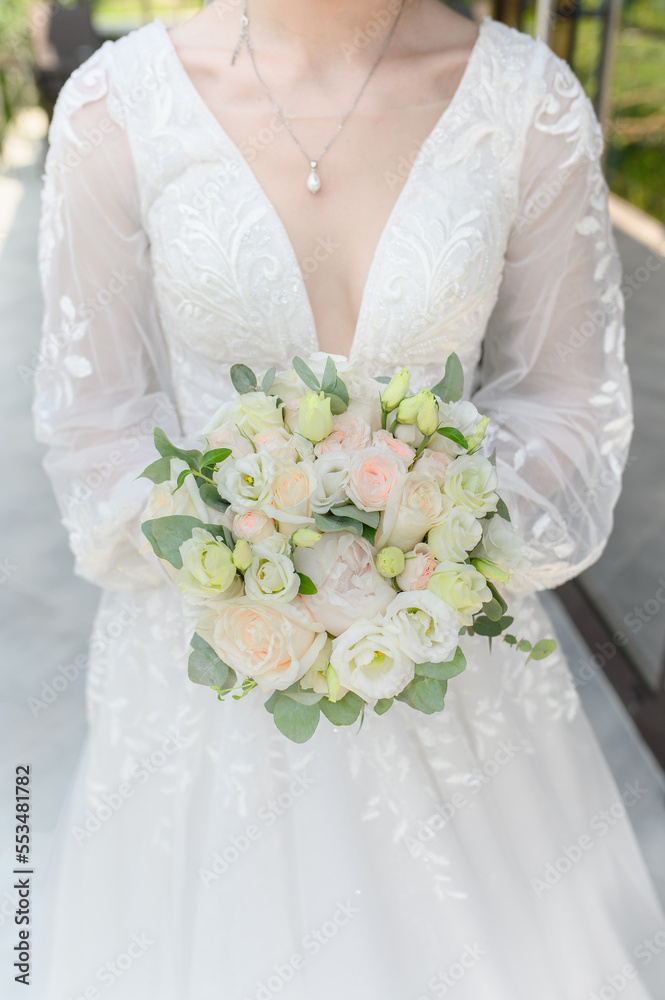 The bride in a beautiful wedding dress holds in front of her a wedding bouquet of roses, freesia. Wedding day.
