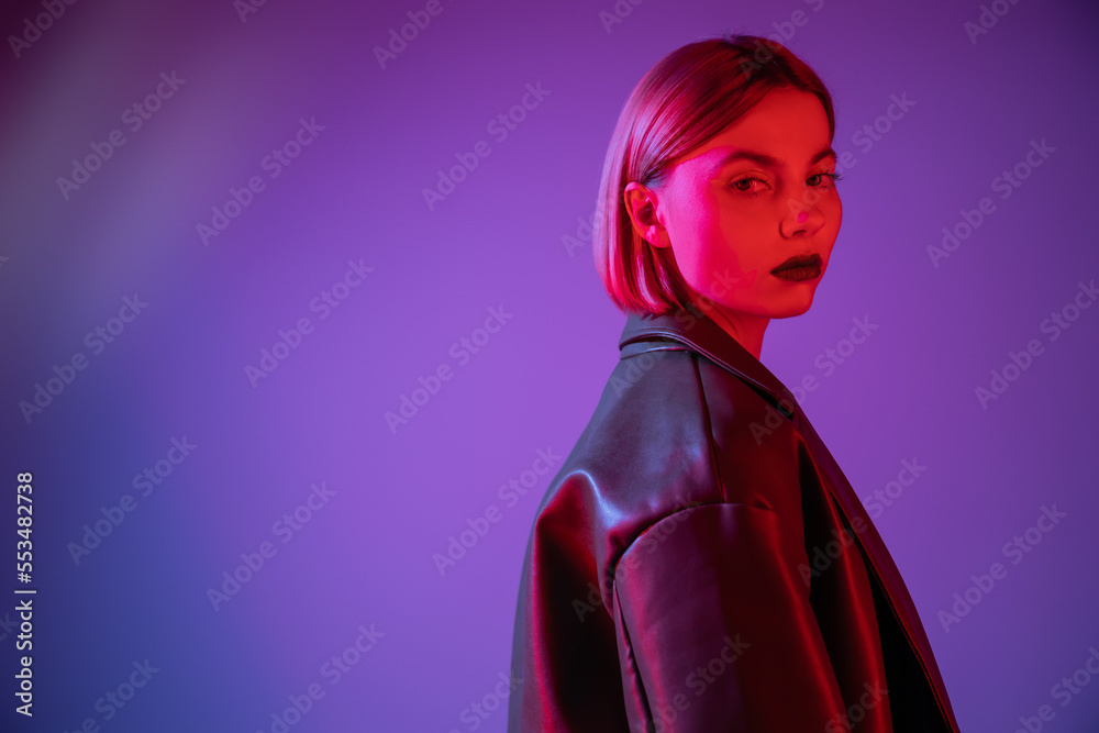 young and stylish woman looking at camera in red light on purple and blue background.