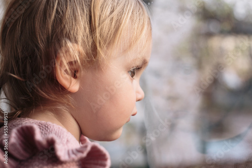 A little girl looks out the window and waits for her mother. Close-up.