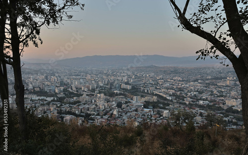View of Tbilisi City from the mountain, Mtatsminda park, on the sunset throw the trees