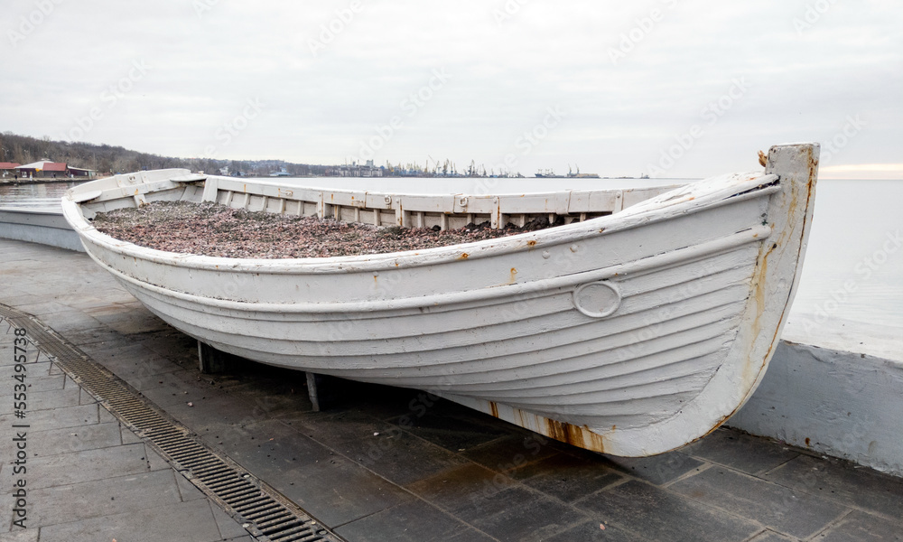 Naklejka premium old rusty wooden white boat on a concrete pier at sunset