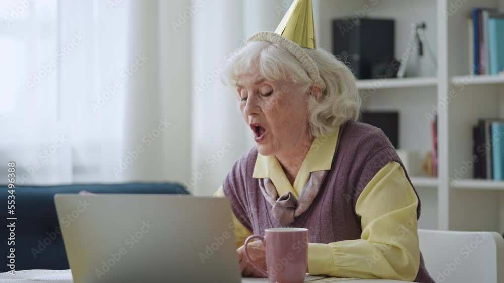 Happy granny sending air kiss and blowing out candles on cake on laptop camera Happy granny sending air kiss and blowing out candles on cake on laptop camera