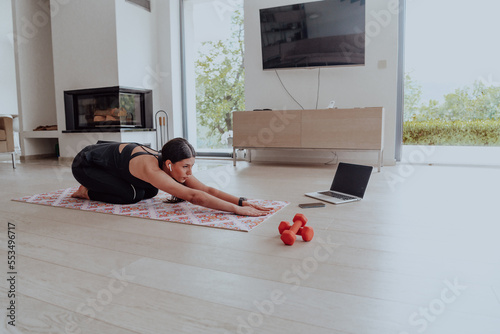 Schilderij op canvas Young Beautiful Female Exercising, Stretching and Practising Yoga with Trainer via Video Call Conference in Bright Sunny House