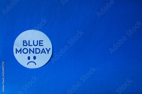 Fondo azul de papel con circulo blanco y blue monday representado con letras y una cara triste el dia mas triste del año 
