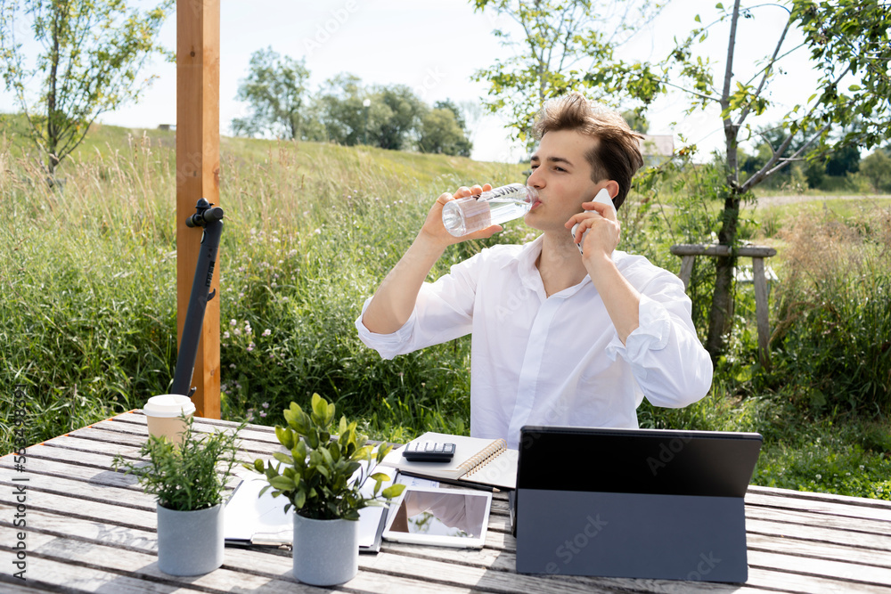 Fototapeta premium young attractive man working or studying in park and sitting by wooden table