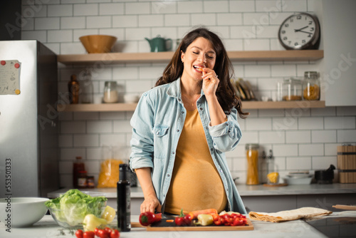 Young woman in kitchen. Beautiful pregnant woman making salad..