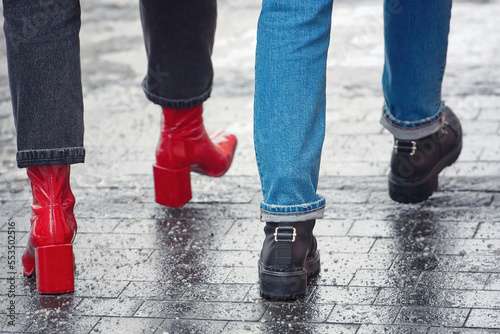 Female couple walking on slippery paving stones sprinkled with rock salt. Women in red and black boots walk on salted sidewalk. Salted sidewalk, paving slab covered with salt, road reagents, melt ice