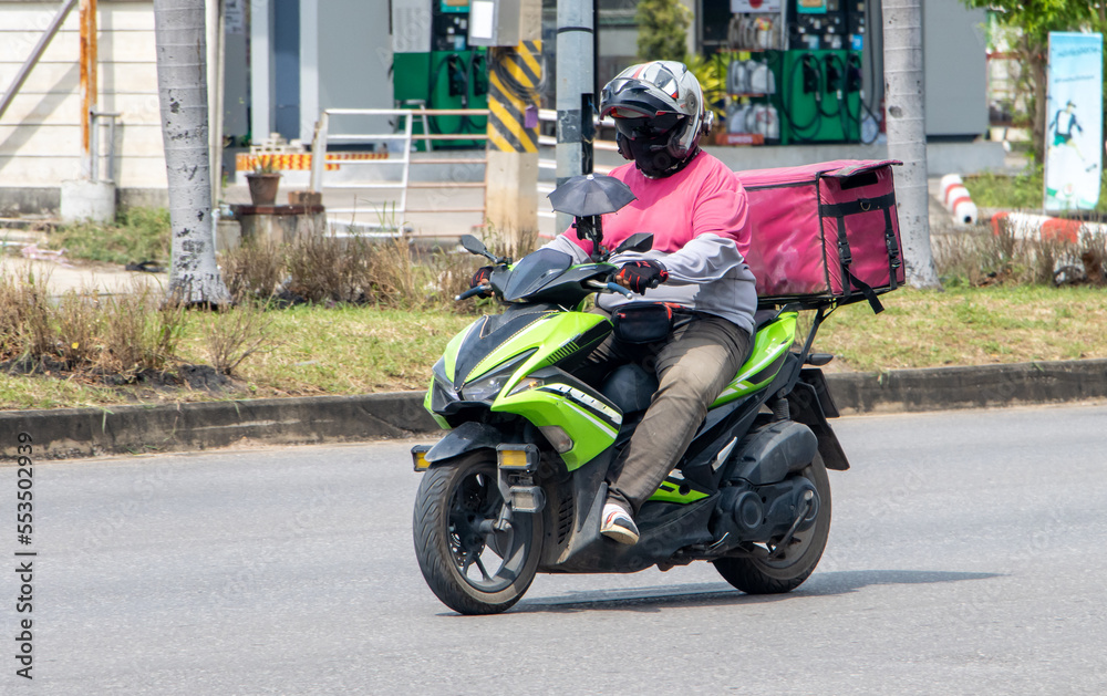 A delivery worker rides a motorcycle with a delivery box