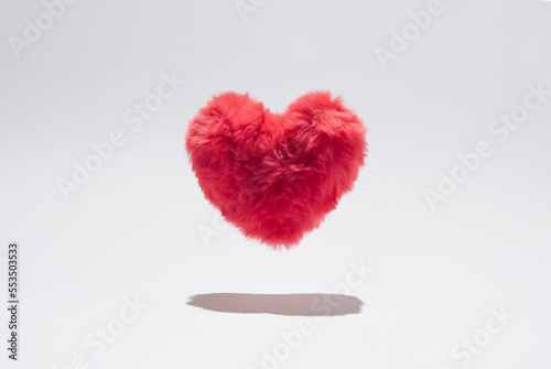 Pink fluffy plush heart levitating above white background.