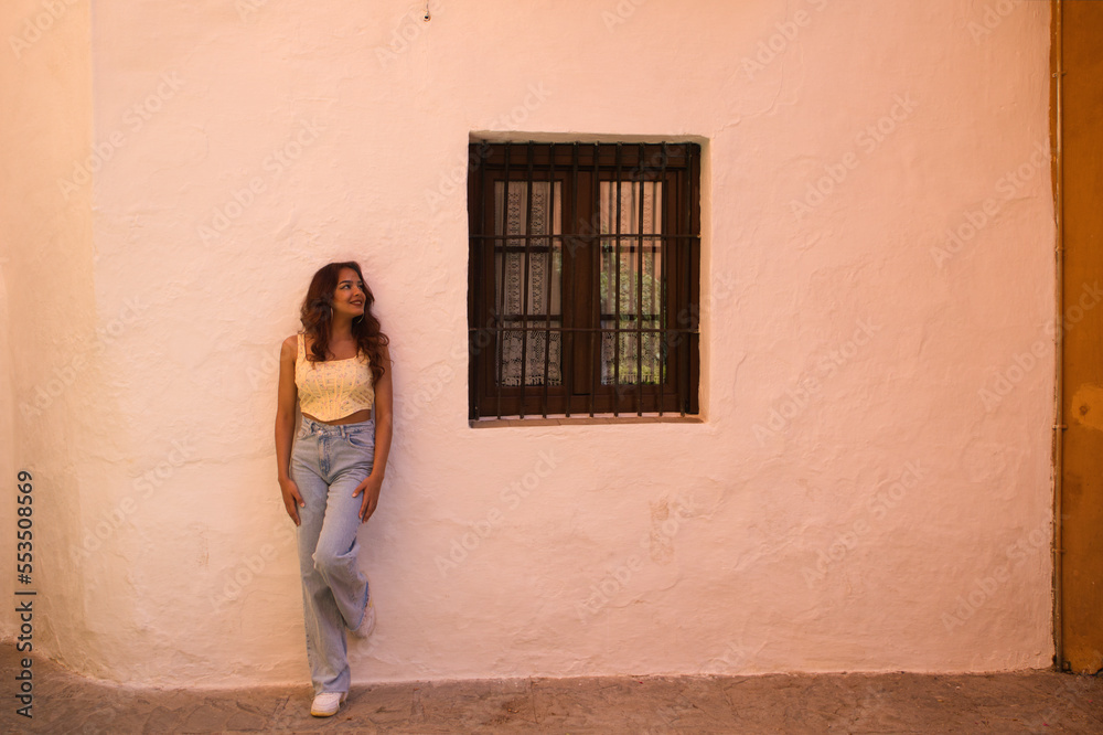 Young beautiful woman dressed in casual clothes leaning against a white wall of an old house in seville. The woman is making different expressions and postures and is enjoying her holidays.