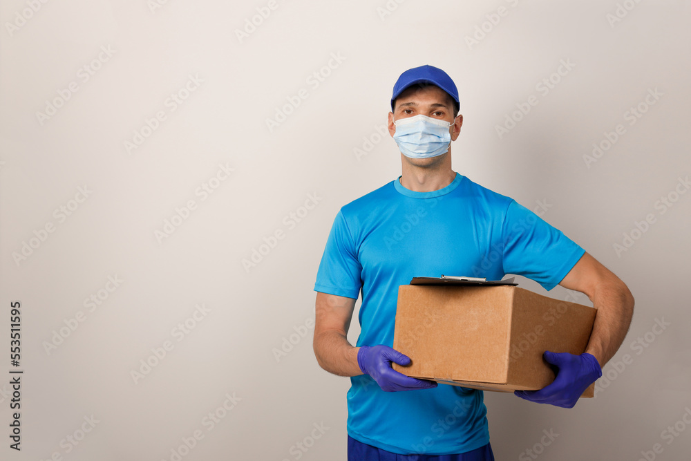 Portrait of handsome attractive delivery man in a medical mask and gloves holding card-board box. Express delivery service. Copy space. Portrait of handsome attractive delivery man in a medical mask and gloves holding card-board box. Express delivery service. Copy space.