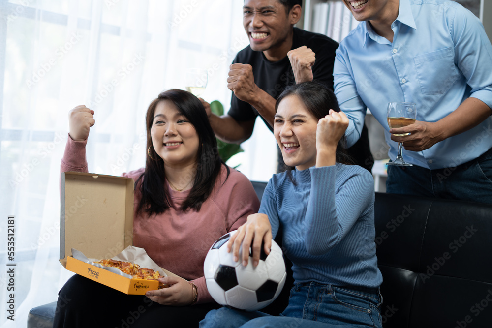 Group of Asian man and woman friends watching soccer games world cup competition on television with eating snack together at home. Sport fans people shouting and celebrating sport team victory match. Group of Asian man and woman friends watching soccer games world cup competition on television with eating snack together at home. Sport fans people shouting and celebrating sport team victory match.