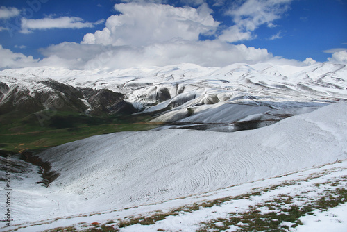 Panorama on the snow-covered plateau of Assy with snow-covered mountain ranges, green areas of the mountains, with the sky and beautiful clouds