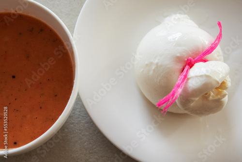 Italian cheese Burrata and a red tomato soup on kitchen table, top view