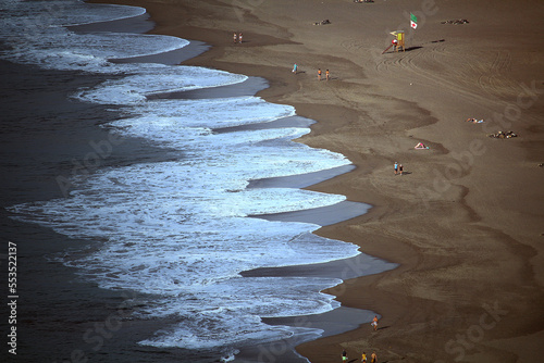 Aerial view at sandy beach at the ocean with big waves and people relaxing (Tejita beach, Tenerife, Spain) photo