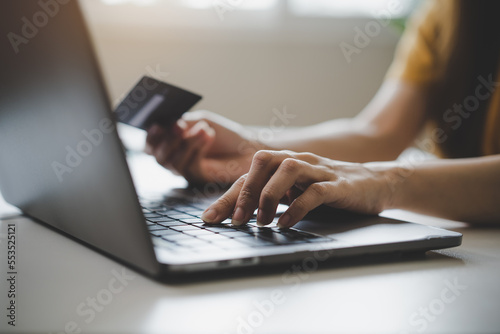 Close up view hands of young woman holding a credit card and doing bank transactions via laptop computer at home