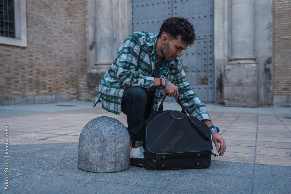 Male musician opening his suitcase on the street to start playing his horn.