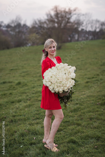 Woman in red dress  holding flowers big bouquet white flowers roses. blooming flowers green natural  background, pastel and soft bouquet floral card.