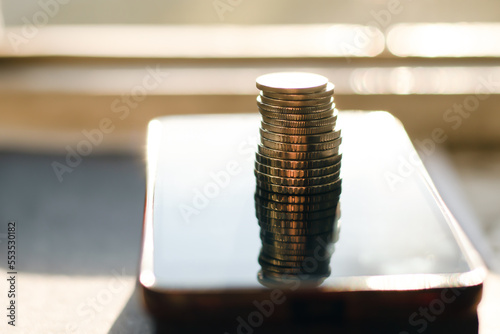 A column of metal coins on a smartphone on a bright sunny day. Close-up with a blurred background.
