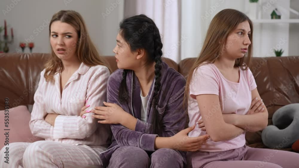 Young Asian woman talking to argued Caucasian friends forcing ladies making peace shaking little fingers. Satisfied happy lady smiling as women gesturing pinky swear sitting on couch in pajamas Young Asian woman talking to argued Caucasian friends forcing ladies making peace shaking little fingers. Satisfied happy lady smiling as women gesturing pinky swear sitting on couch in pajamas