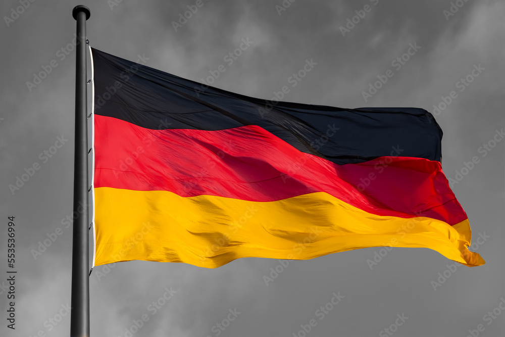 German Flag in black-red-gold colors as national Symbol of the Bundesrepublik Deutschland. Background in black and white greyscale contrasting the isolated colorful hoisted bannner waving in the wind German Flag in black-red-gold colors as national Symbol of the Bundesrepublik Deutschland. Background in black and white greyscale contrasting the isolated colorful hoisted bannner waving in the wind
